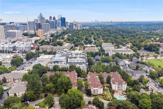 Aerial panoramic view of a city with various buildings, lush green trees, and a distant skyline.