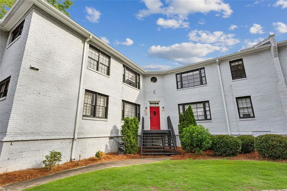 Front view of a two-story white brick building with a red door and black windows.