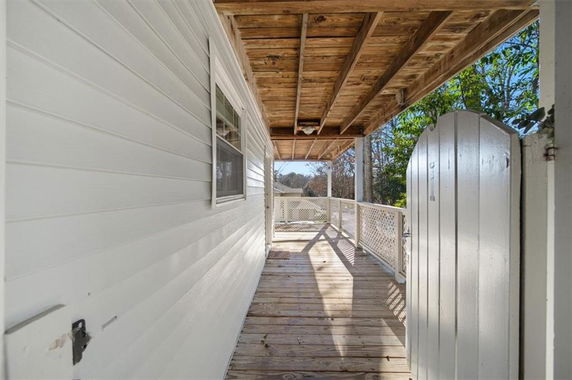 Wooden exterior corridor of a house with white siding and railing.