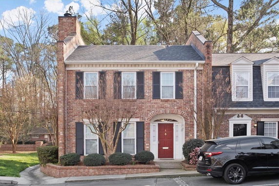 Front view of a two-story brick townhouse with a red door and black shutters.