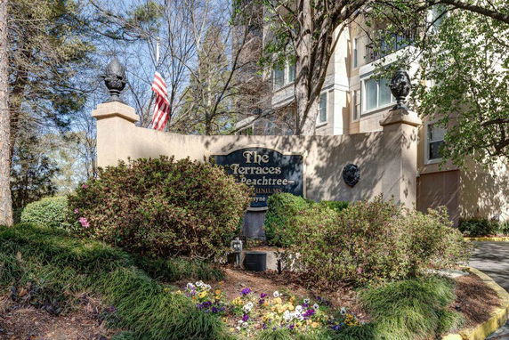 Front view of a condominium building entrance with a sign and landscaping.