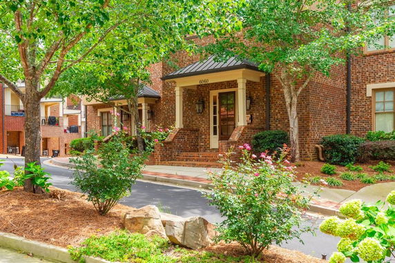 Front view of a brick townhouse with a small porch and surrounding greenery.