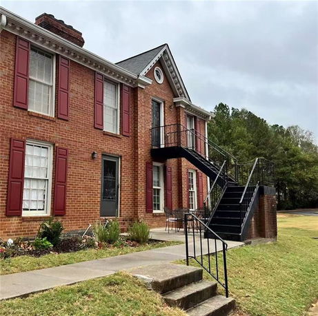 Front view of a brick house with red shutters and an external staircase.