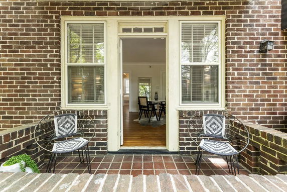 Front view of a brick house with a small patio area and two chairs.
