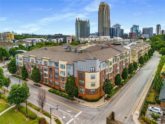 Aerial view of a multi-story apartment building with a modern design, surrounded by tree-lined streets.