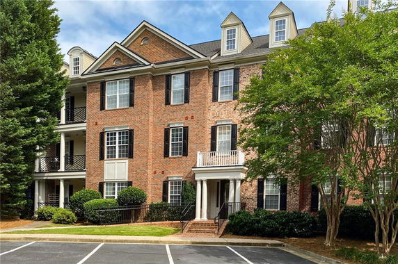 Front view of a multi-story brick apartment building with dormer windows and a small front entry porch.