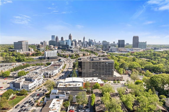 Panoramic view of a cityscape with numerous buildings, roads, and green areas under a clear blue sky.
