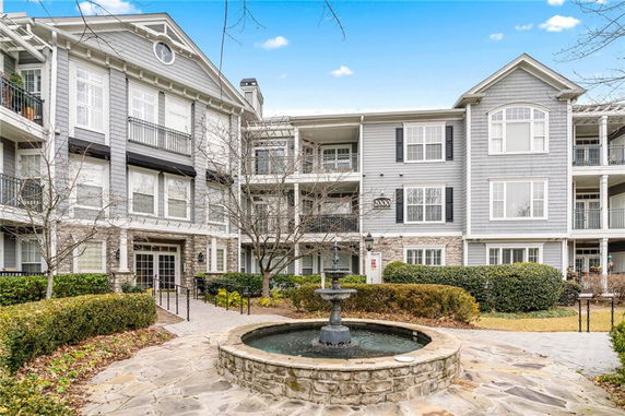 Front view of a multi-story residential building with balconies and a water fountain in front.