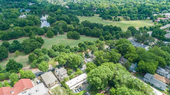 Aerial panoramic view of a neighborhood with houses and a large green park surrounded by trees.