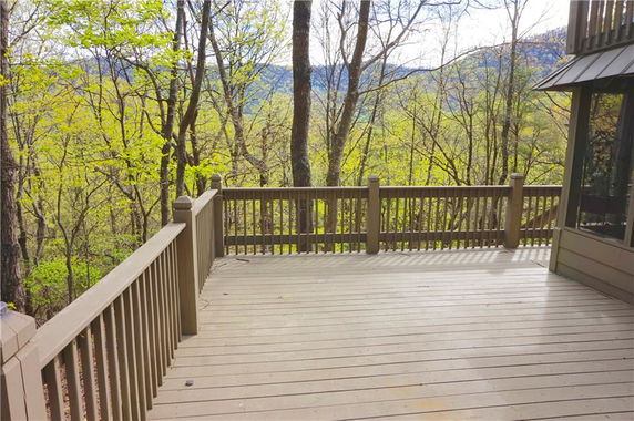 Wooden deck with railing overlooking a forest and distant hills.