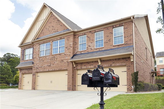 Front view of a two-story brick house with three garages and multiple mailboxes in front.