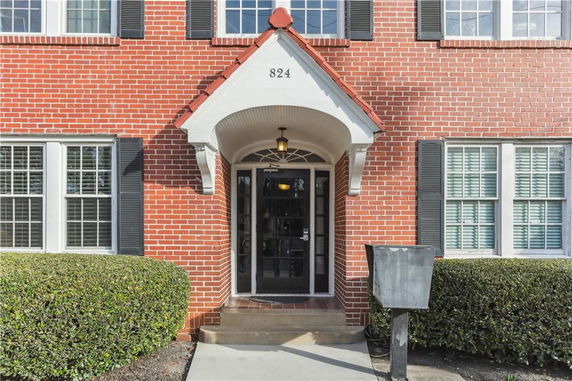 Front view of a brick building entrance with arched doorway and windows with shutters.