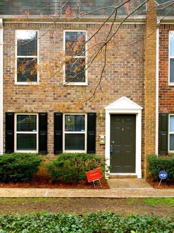 Front view of a brick townhouse with black shutters and a black door.