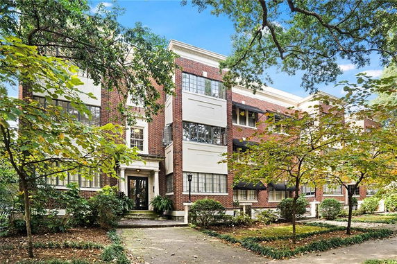Front view of a multi-story brick building with large windows and entrance surrounded by trees.
