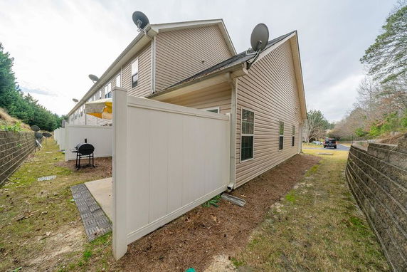Side view of a tan house with multiple satellite dishes on the roof and a privacy fence.
