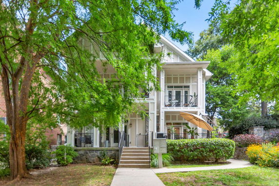 Front view of a two-story house with a porch and balcony, surrounded by greenery.