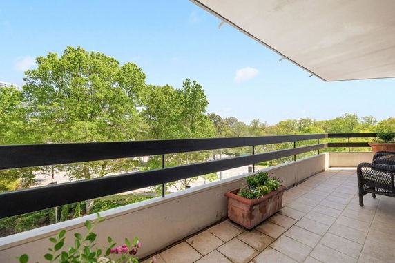 View from a balcony with railings and outdoor furniture overlooking trees and a street.