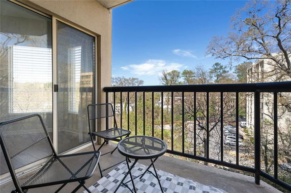 Balcony view with outdoor chairs and a table overlooking trees and buildings in the distance.