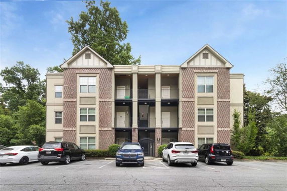 Front view of an apartment building with three levels and parking spaces in front.