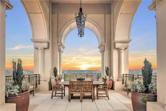 Exterior view of a terrace with arched columns and outdoor seating, overlooking a sunset.