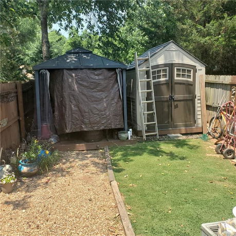 Outdoor view of a small storage shed and covered structure in a backyard.