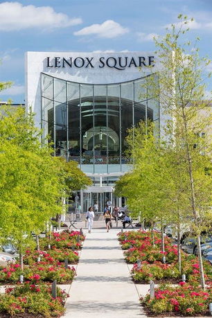 Front view of a modern multi-story shopping mall entrance with glass facade and floral landscaping.