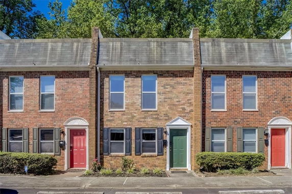 Front view of a two-story brick townhouse with contrasting colored doors and windows with shutters.