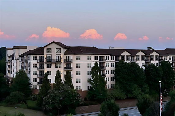 Front view of a multi-story apartment building with balconies and a sloped roof.