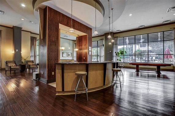 Interior view of a club house area with a bar counter and seating, featuring a pool table and large windows.