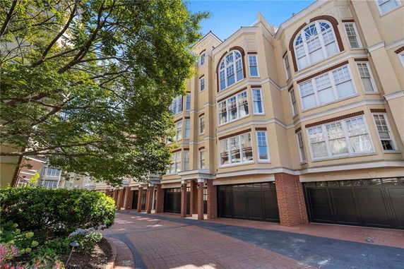 Front view of a multi-story residential building with large windows and a brick facade at the ground level.
