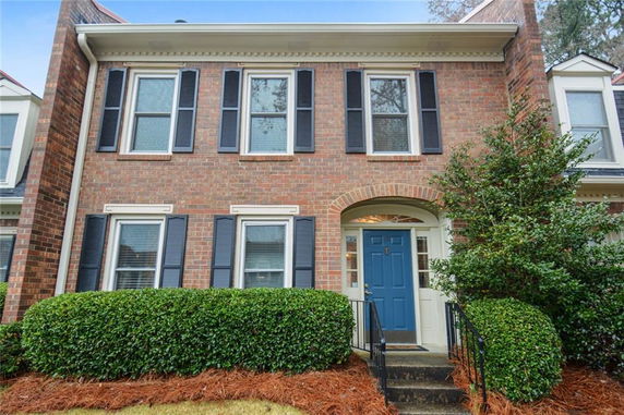 Front view of a two-story brick townhouse with a blue door and black shutters.