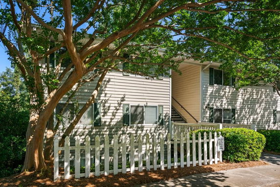 Front view of a multi-story building with a white picket fence and surrounding trees.