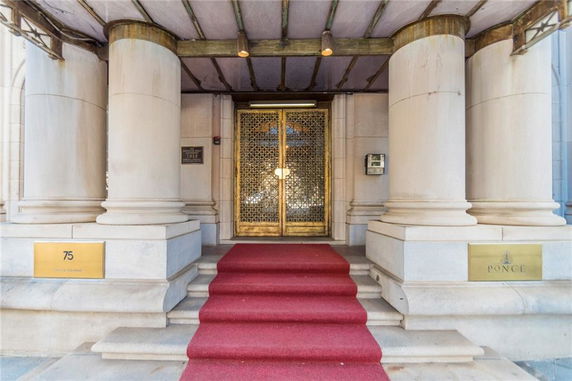 Entrance of a building with large columns and a red carpet leading to ornate doors.
