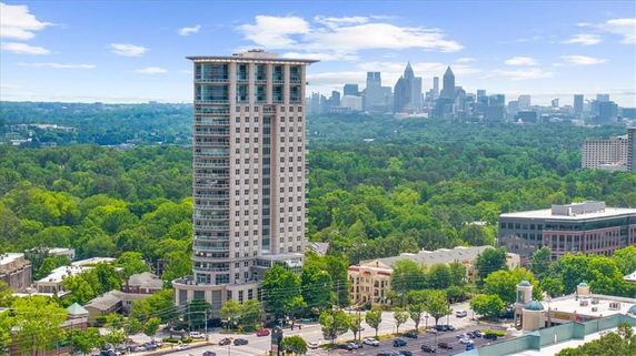 Elevated view of a tall cylindrical building surrounded by greenery and cityscape in the background.