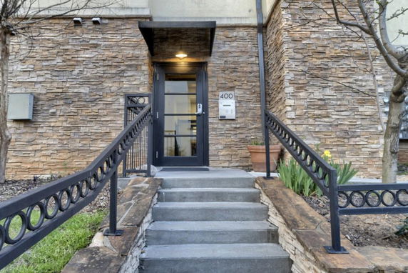 Front view of a building entrance with stone wall facade and metal railings.