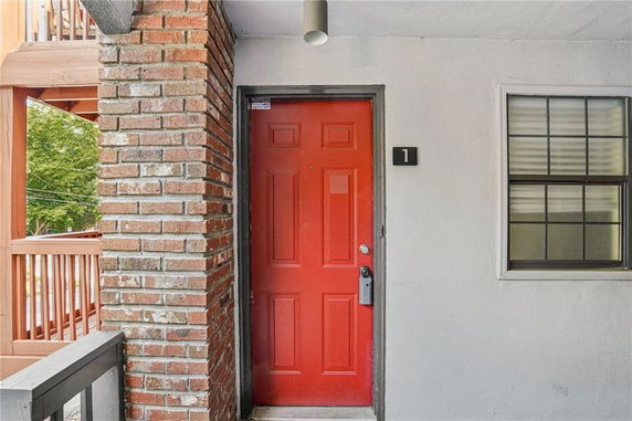 Front view of a building entrance with a red door and brick pillar.