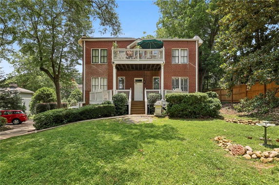 Front view of a two-story brick house with balcony and stairs leading to entrance.
