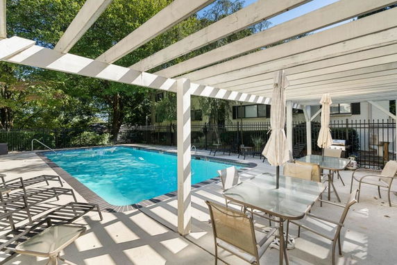 Outdoor swimming pool area with patio chairs and tables under a pergola.