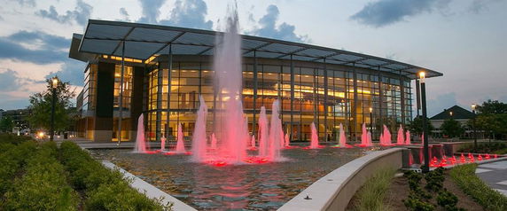 Front view of a modern building with glass facade and illuminated water fountains in front.