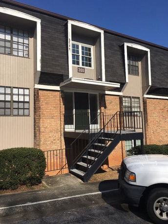 Front view of a multi-story residential building with brick and vertical siding and exterior stairs leading to an upper floor.