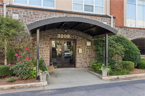 Front view of a stone building entrance with arched canopy and double glass doors.