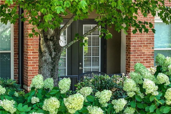 Front view of a brick house with a porch and greenery.