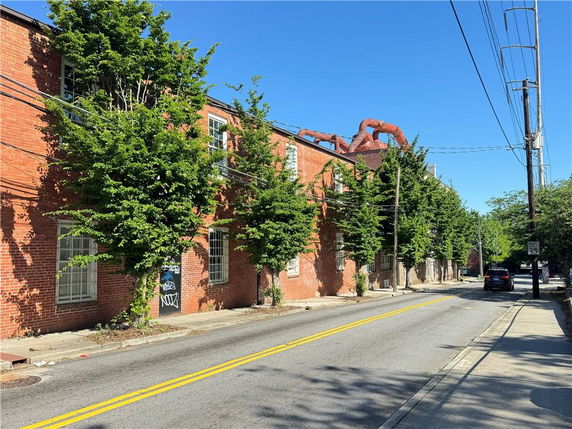 Front view of a brick building with several windows and trees along the sidewalk.