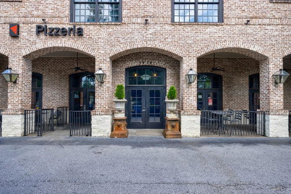 Front view of a brick-clad building with arches and a pizzeria sign.