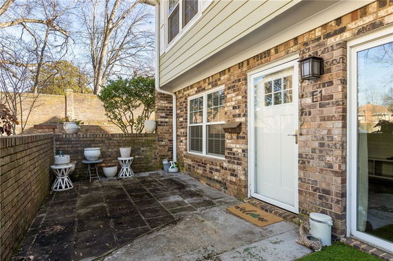 Side view of a brick house with a glass door and window, small outdoor tiled area and potted plants.