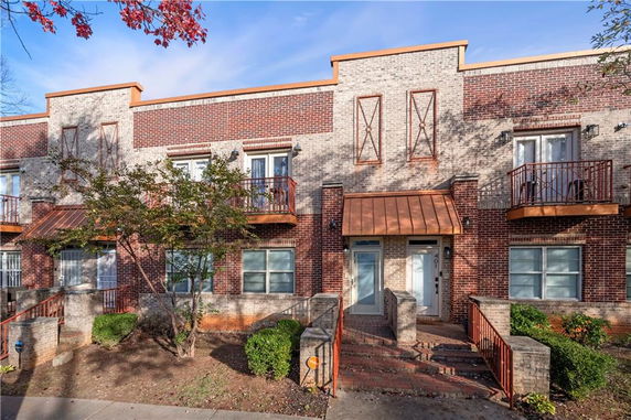 Front view of a two-story brick townhouse with small balconies and a central entrance.