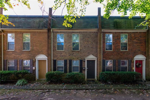 Front view of a row of brick townhouses with small shrubs in front.