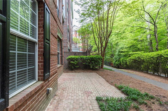 Side view of a brick building with windows and a paved area, surrounded by trees and shrubs.