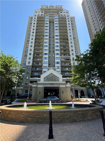Front view of a multi-story residential building with balconies and a landscaped entrance.