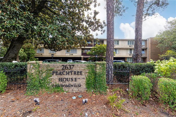 Front view of a multi-story condominium building with a brick sign labeled 'Peachtree House Condominiums'.